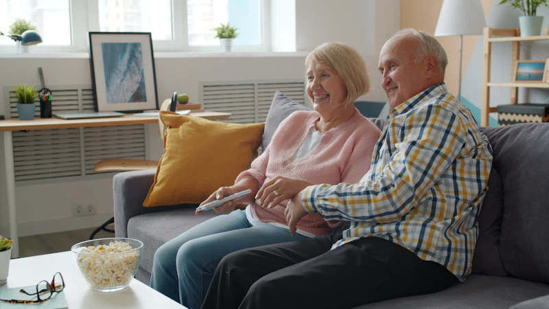 Älteres Ehepaar sitzt lachend auf dem Sofa und schaut fern