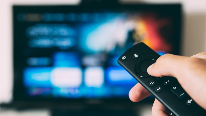 Hand mit Fernbedienung vor einem unscharfen Fernsehbildschirm
