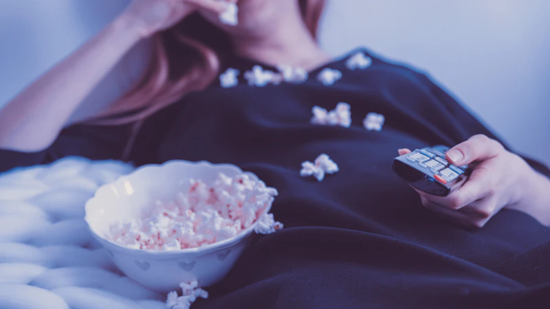 Frau schaut abends mit Popcorn fern und hält die Fernbedienung